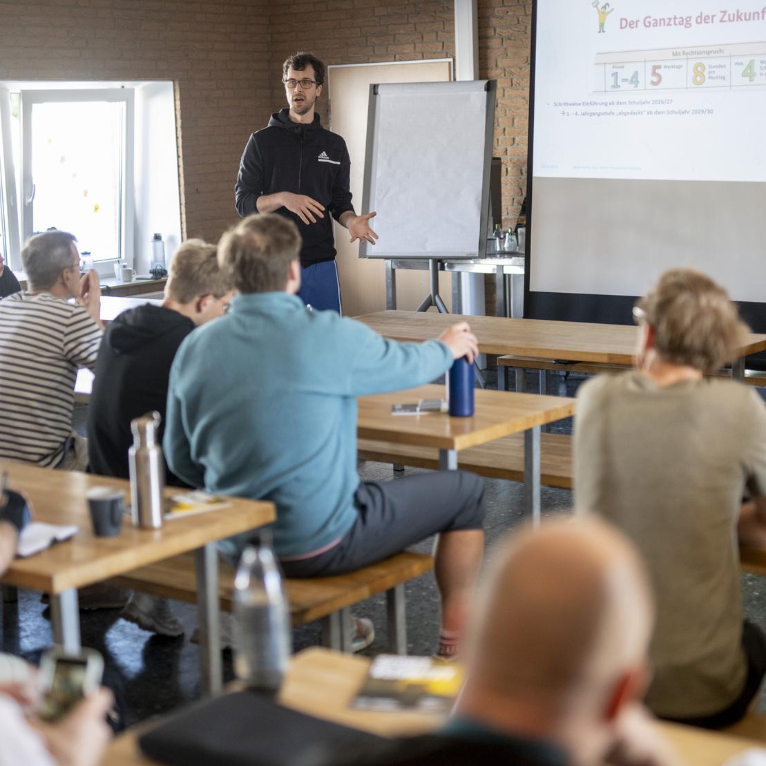 Vortragssituation in einem Seminarraum mit einer Person, die vor Teilnehmern eine Pr&auml;sentation h&auml;lt.