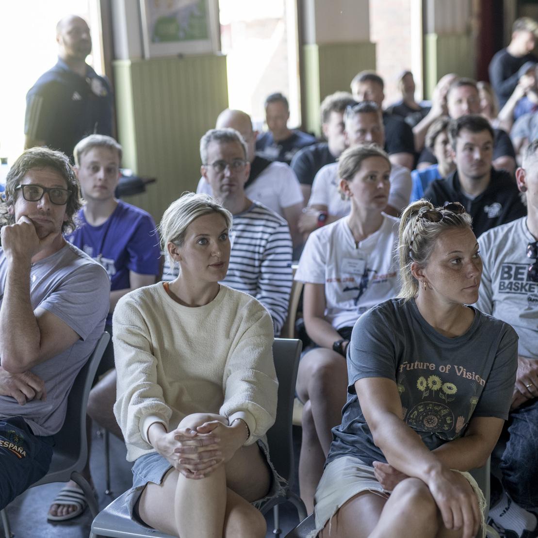 Eine Gruppe von Menschen sitzt aufmerksam in einem Raum und h&ouml;rt einem Vortrag zu.