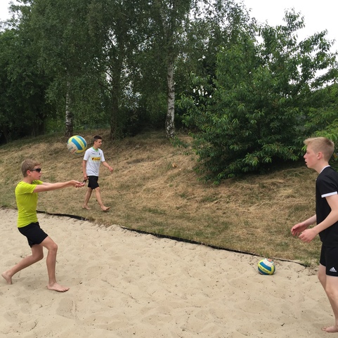 Drei Kinder spielen Beachvolleyball auf einem Sandplatz, w&auml;hrend ein Ball in der Luft fliegt.