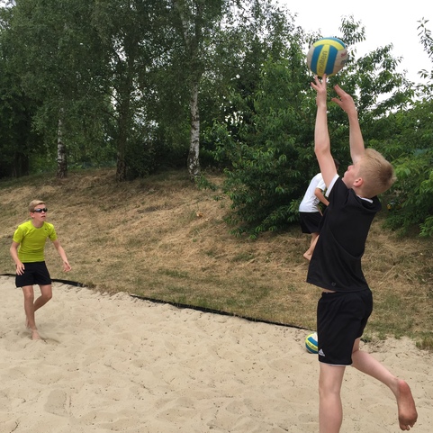 Zwei Kinder spielen im Sand mit einem Volleyball; eins wirft den Ball, das andere steht bereit zum Fangen.
