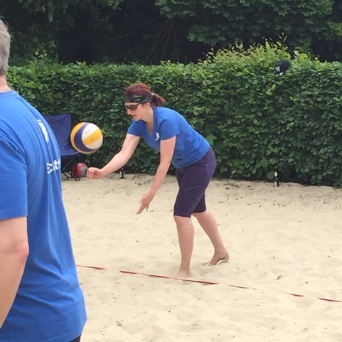 Eine Frau in blauer Sportswear spielt Beachvolleyball und bereitet sich auf den Aufschlag im Sand vor.