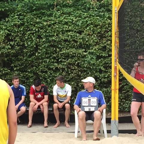 Gruppe von vier Personen in sportlicher Kleidung auf einem Sandplatz, neben einem Schiedsrichterstuhl mit Punktestand.