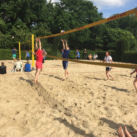 Zwei Spieler springen am Netz, um einen Volleyball in einem Sandvolleyballspiel im Freien zu erreichen.