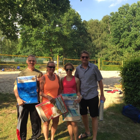 Vier Personen stehen auf Rasenfl&auml;che in Sportkleidung, halten Plakate vor einem Volleyballfeld in einem Park.