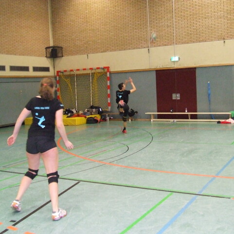 Drei Sportlerinnen spielen Handball in einer Halle, eine wirft den Ball, w&auml;hrend die anderen sich positionieren.