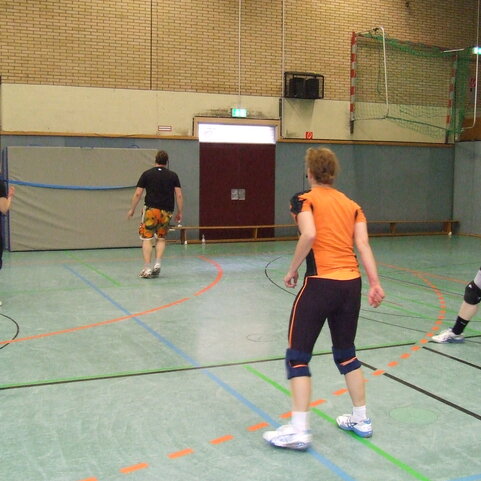 Vier Personen in sportlicher Bekleidung stehen auf einem Hallenboden und spielen eine Runde Volleyball.