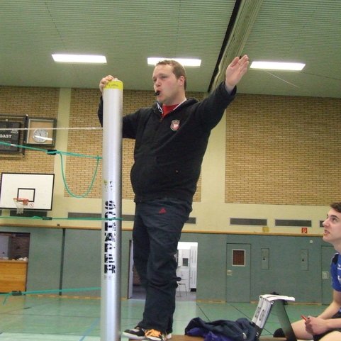 Ein Trainer steht auf einer Bank und gibt Anweisungen, w&auml;hrend ein Spieler auf der Bank zusieht.