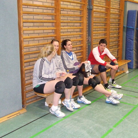 Vier Sportler sitzen auf einer Bank in einer Turnhalle, w&auml;hrend sie sich entspannen und miteinander sprechen.