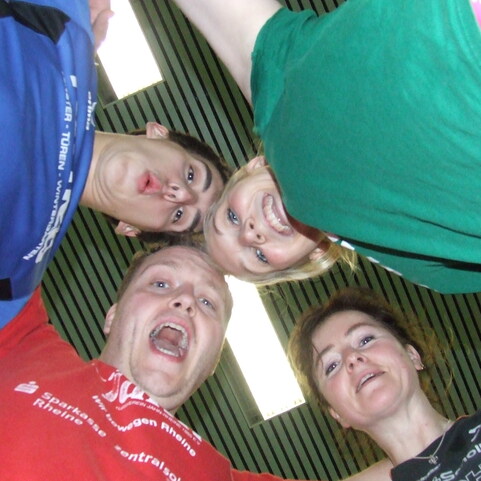 Vier Personen standen im Kreis und schauen nach unten, ein fr&ouml;hliches L&auml;cheln zeigt ihre Gesichter.