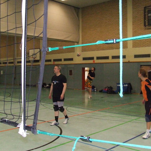 Drei Volleyballspieler in einer Halle, einer empf&auml;ngt einen Ball, w&auml;hrend zwei andere bereit stehen.