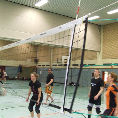 Volleyballspieler in einer Halle beim Training, ein Ball fliegt &uuml;ber das Netz, Spieler in verschiedenen Positionen.