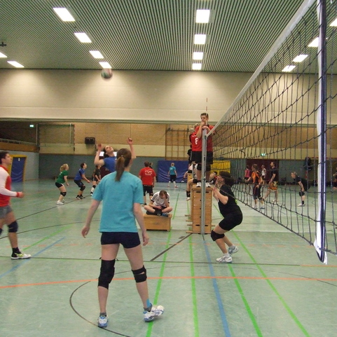 Volleyballtraining in einer Halle mit mehreren Spielern, einem Netz und einem Ball, der in der Luft fliegt.