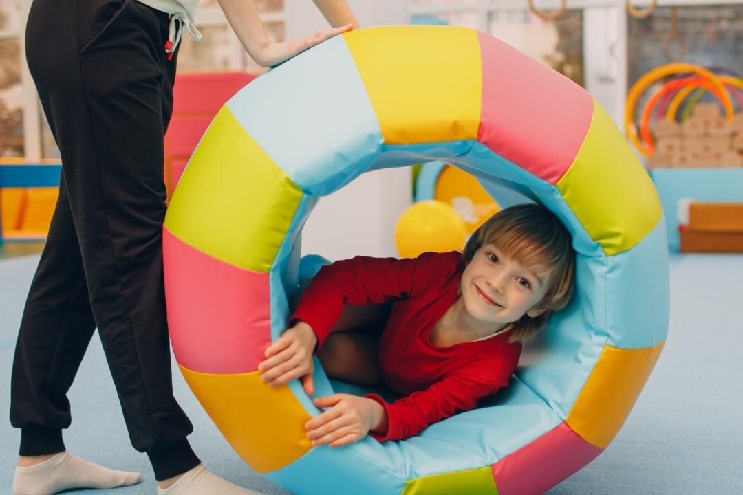 Kind mit fr&ouml;hlichem Gesicht kriecht durch einen bunten Schaumstoffring in einem Indoor-Spielraum.