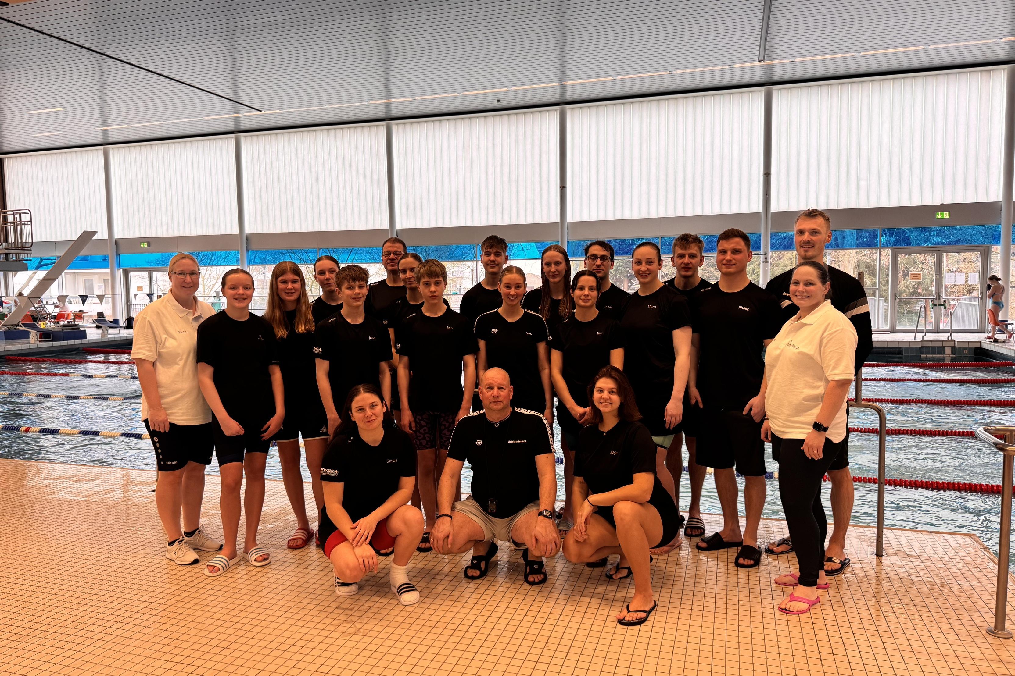 Gruppe von Schwimmern in schwarz gestreiften T-Shirts steht am Beckenrand eines Schwimmbads.