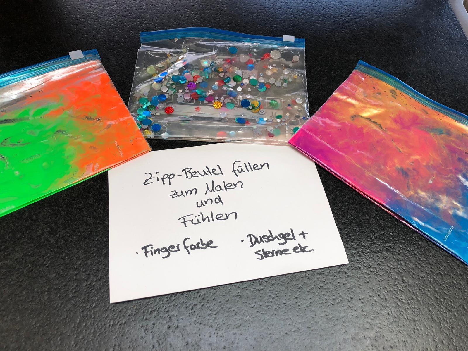Drei gef&uuml;llte Zipp-Beutel mit bunten Materialien und einer Anleitung zum Malen und F&uuml;hlen auf einem Tisch.