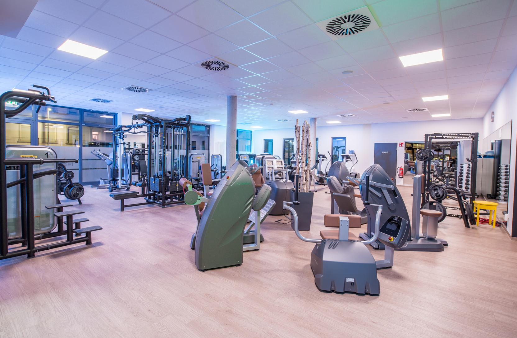 Moderne Fitnessstudio-Ausstattung mit verschiedenen Trainingsger&auml;ten und freien Gewichten in einem hellen Raum.
