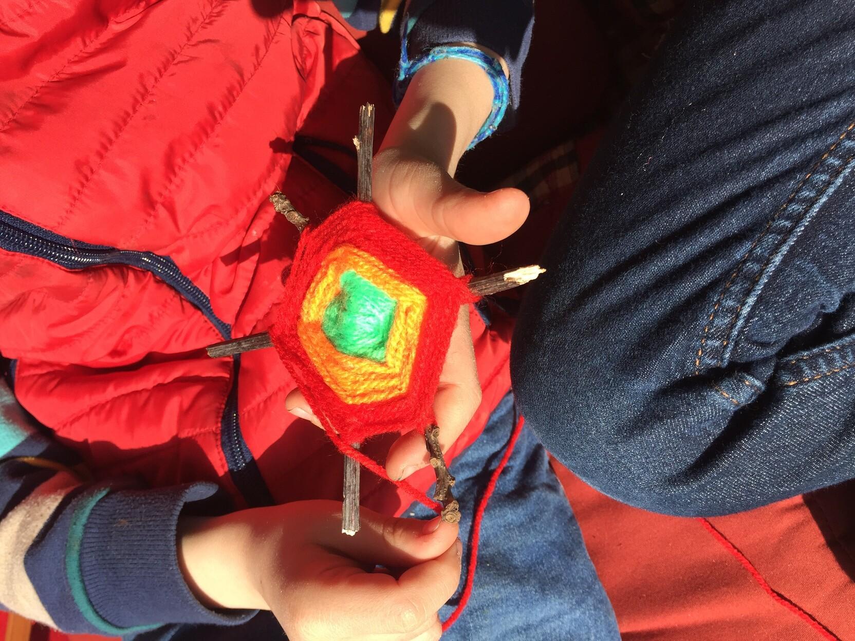 Ein Kind h&auml;lt eine handgefertigte, farbige Wollweberei mit Holzst&auml;ben in den H&auml;nden.