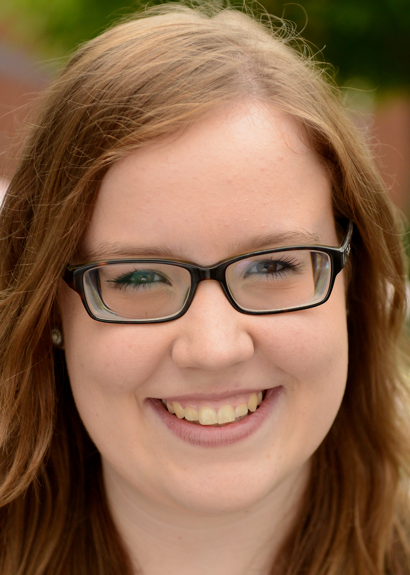 Portr&auml;t einer l&auml;chelnden Frau mit Brille und lockigem, braun-blondem Haar, umgeben von gr&uuml;ner Natur.