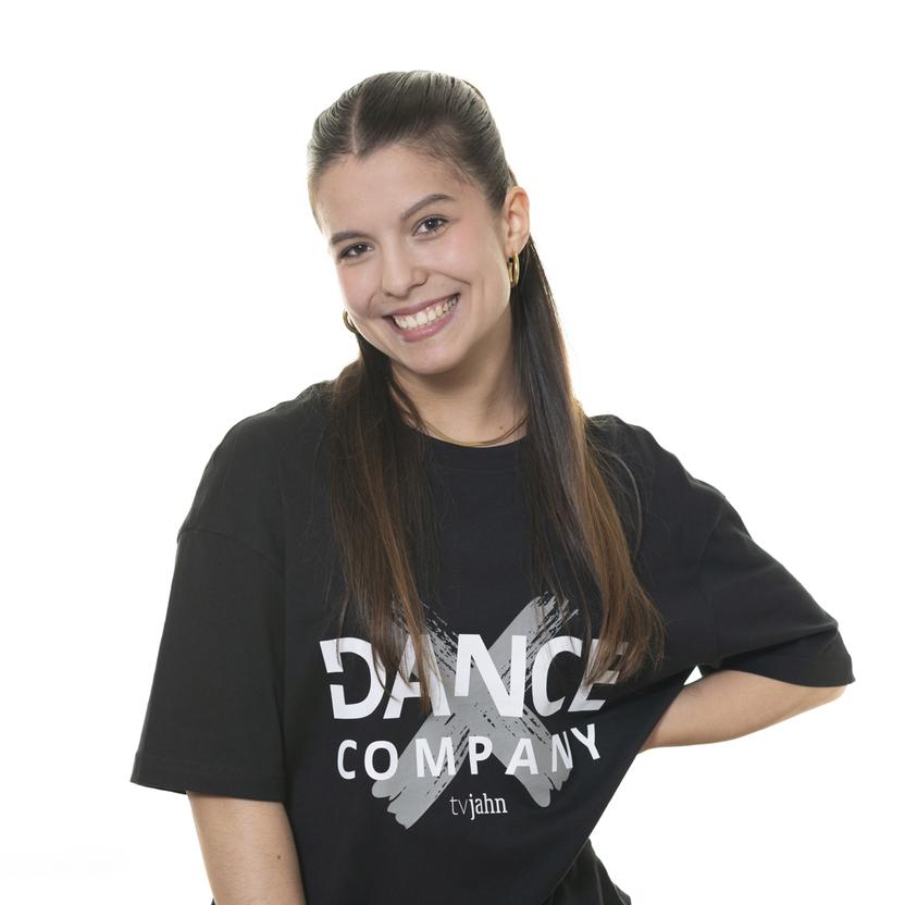 Junge Frau l&auml;chelt in einem schwarzen T-Shirt mit der Aufschrift &bdquo;DANCE COMPANY&ldquo; vor wei&szlig;em Hintergrund.