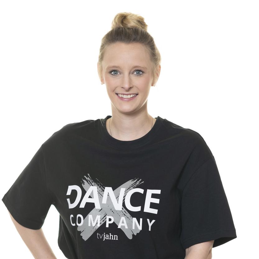 Junge Frau mit hochgestecktem Haar in schwarzem T-Shirt mit Aufdruck &bdquo;DANCE COMPANY&ldquo; posiert vor wei&szlig;em Hintergrund.
