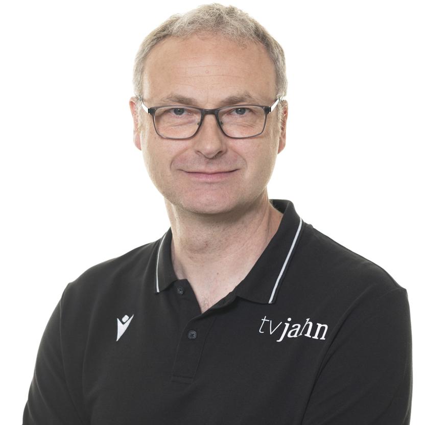 Mann mit Brille und verschränkten Armen trägt ein schwarzes Poloshirt mit dem Logo "tvjahn". Hintergrund ist weiß.