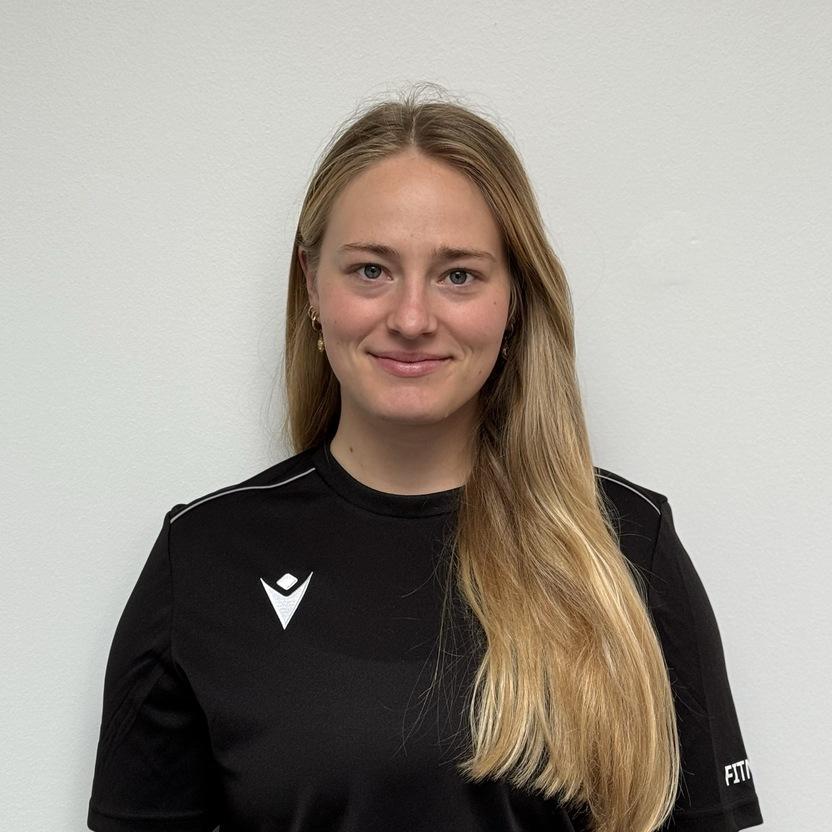 Porträt einer lächelnden Frau mit langen Haaren, die ein schwarzes Sportshirt trägt, vor einem neutralen Hintergrund.
