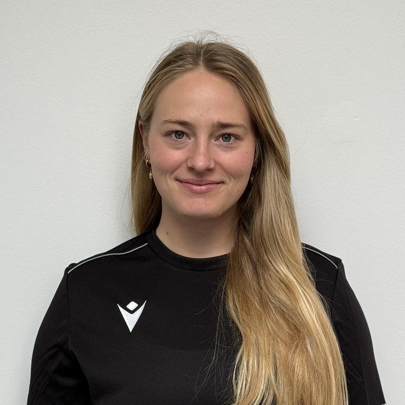 Porträt einer lächelnden Frau mit langen Haaren, die ein schwarzes Sportshirt trägt, vor einem neutralen Hintergrund.