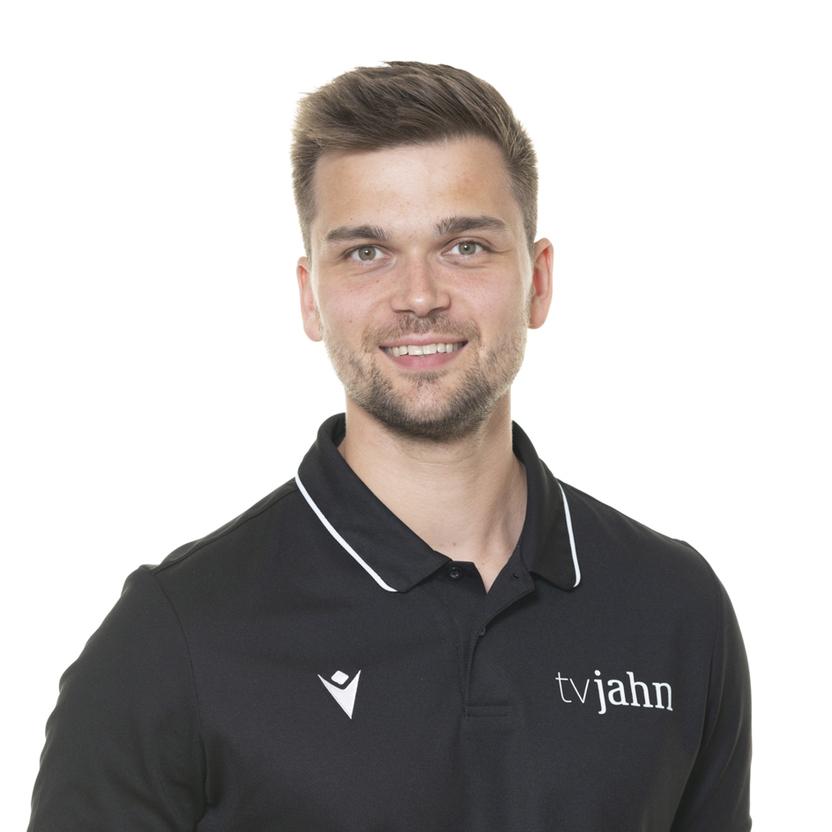 Mann mit kurzem Haar und Lächeln trägt ein schwarzes Poloshirt mit Aufdruck "tvjahn" vor neutralem Hintergrund.