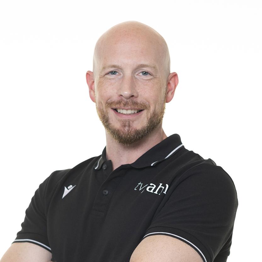 Mann mit kurzem, glattem Haar und Bart lächelt in schwarzem Polo-Shirt vor weißem Hintergrund.