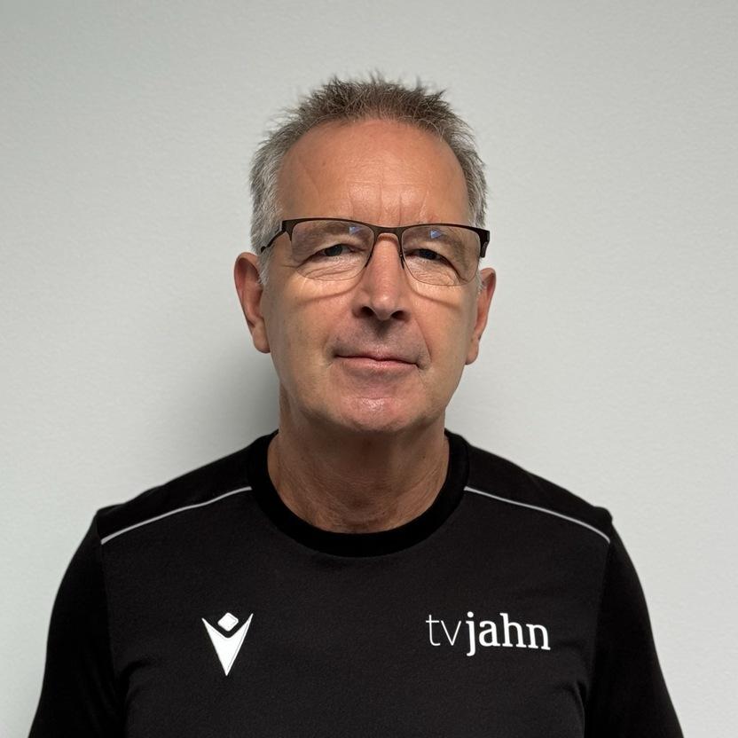 Mann mit Brille in schwarzem Sportshirt steht vor einer weißen Wand.