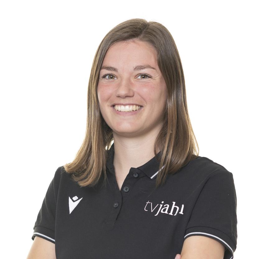 Porträt einer lächelnden Frau mit langen, brünetten Haaren in schwarzem Polo mit Logo, vor weißem Hintergrund.