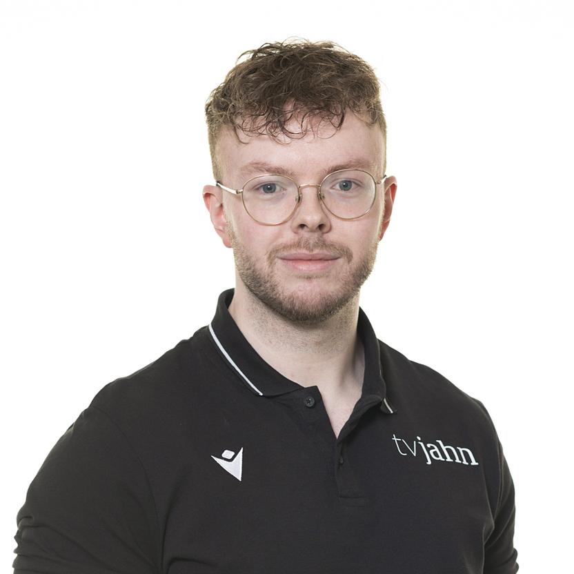 Porträt eines Mannes mit Brille, kurzem Haar und schwarzem Poloshirt mit Logo vor weißem Hintergrund.