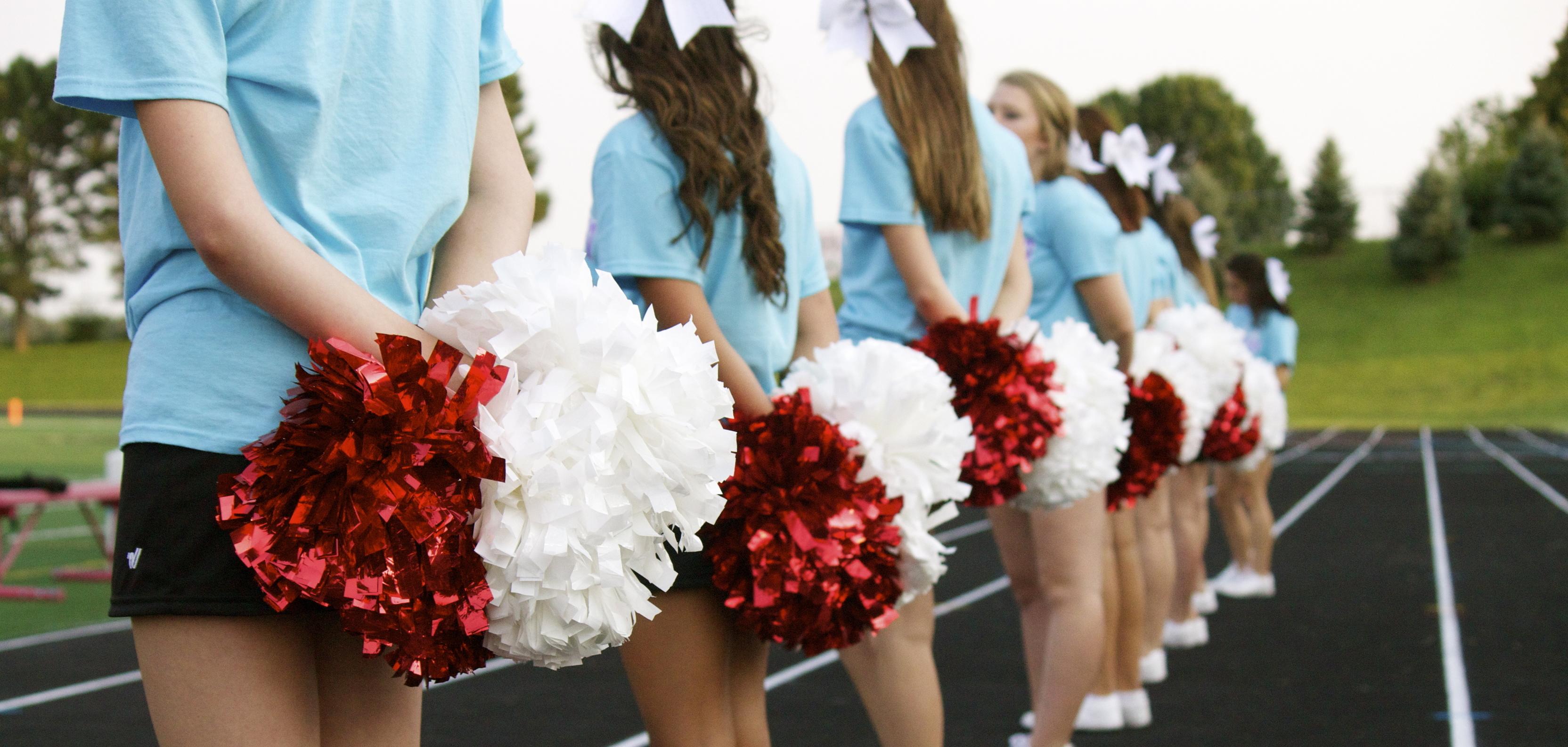 Reihe von Cheerleadern in blauen T-Shirts mit roten und wei&szlig;en Pompons auf einer Laufbahn.