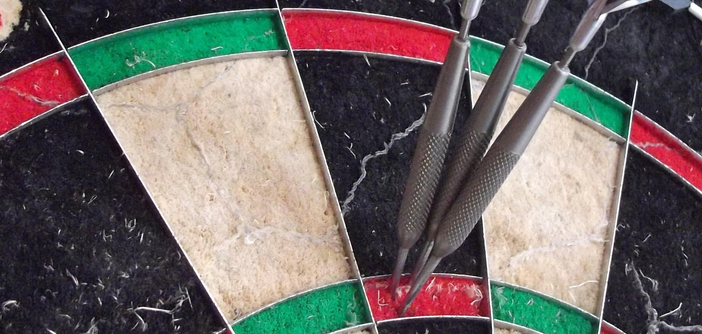 Nahaufnahme eines Dartboards mit drei Pfeilen, die im roten und gr&uuml;nen Bereich stecken.