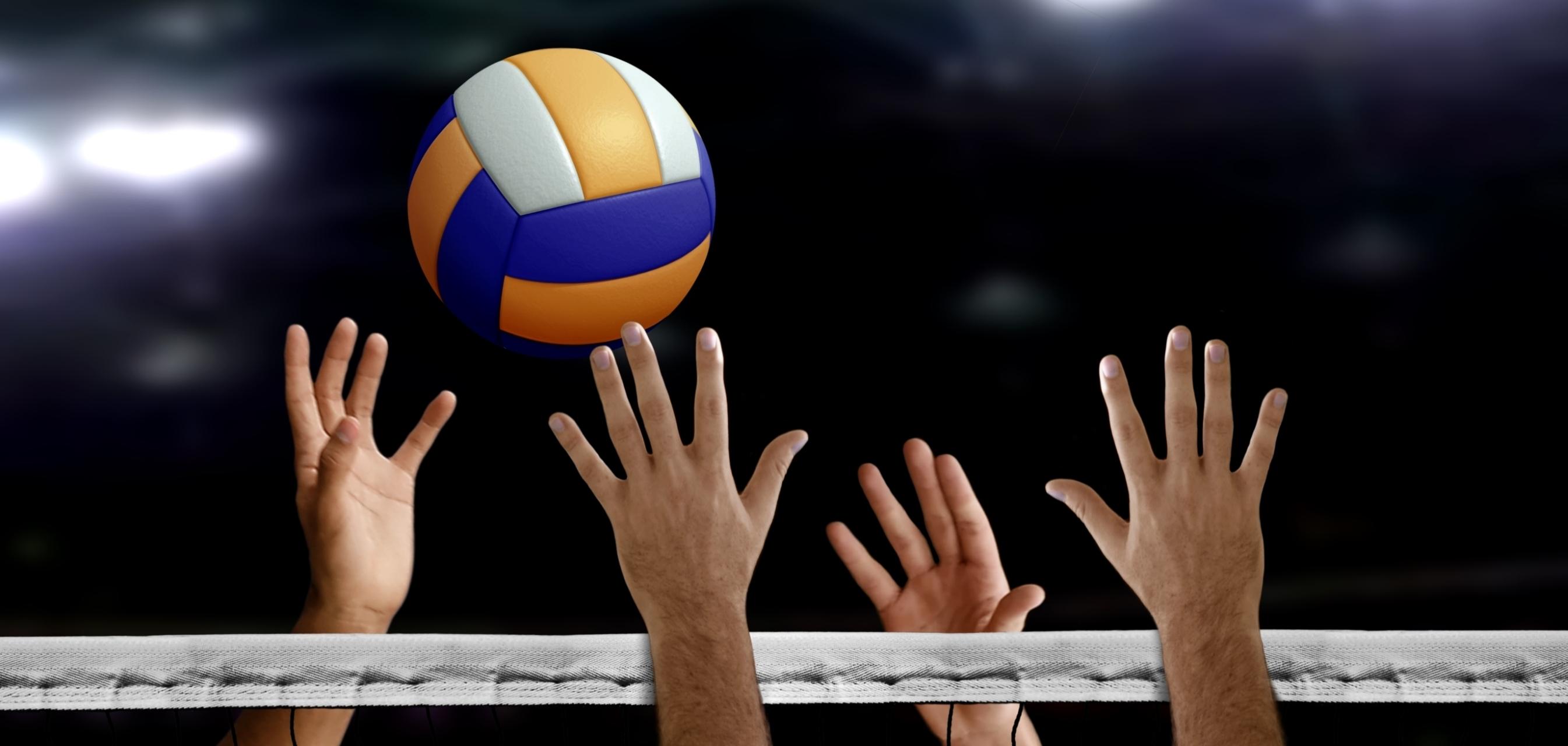 Hände greifen nach einem Volleyball, der über ein Netz in einer Sporthalle fliegt.