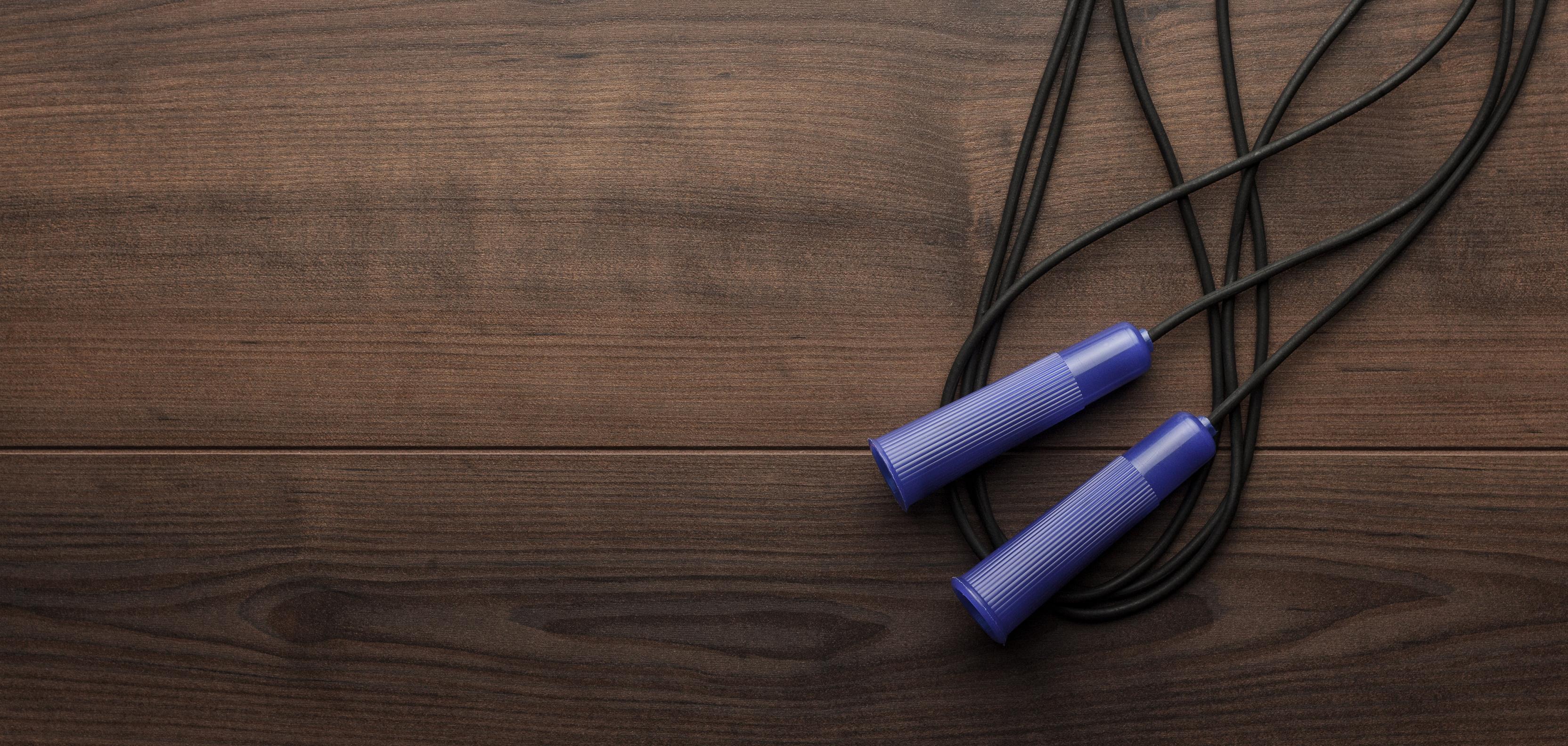 Springseil mit blauen Griffen liegt auf einer dunklen Holzoberfläche.