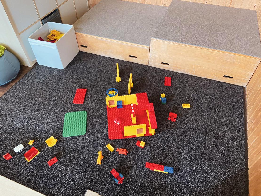 Bunte Baukl&ouml;tze liegen verstreut auf einem Teppich in einer Spielumgebung mit Aufbewahrungsbox.