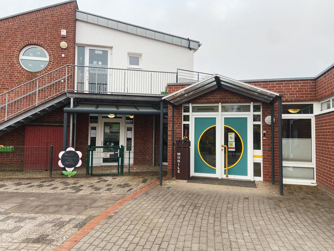 Eingang zu einem modernen Geb&auml;ude mit zwei Eing&auml;ngen, einer geschwungenen Treppe und einer gr&uuml;nen T&uuml;r im Vordergrund.