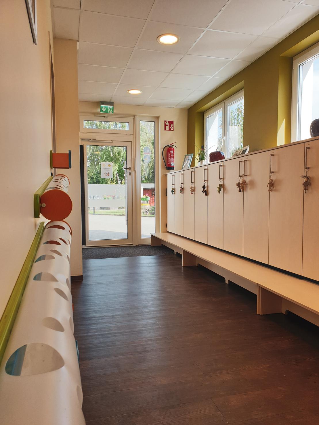 Lichtdurchfluteter Flur mit Schr&auml;nken und Sitzbank, vorne ein Eingang mit gro&szlig;en Fenstern und Sicht ins Freie.