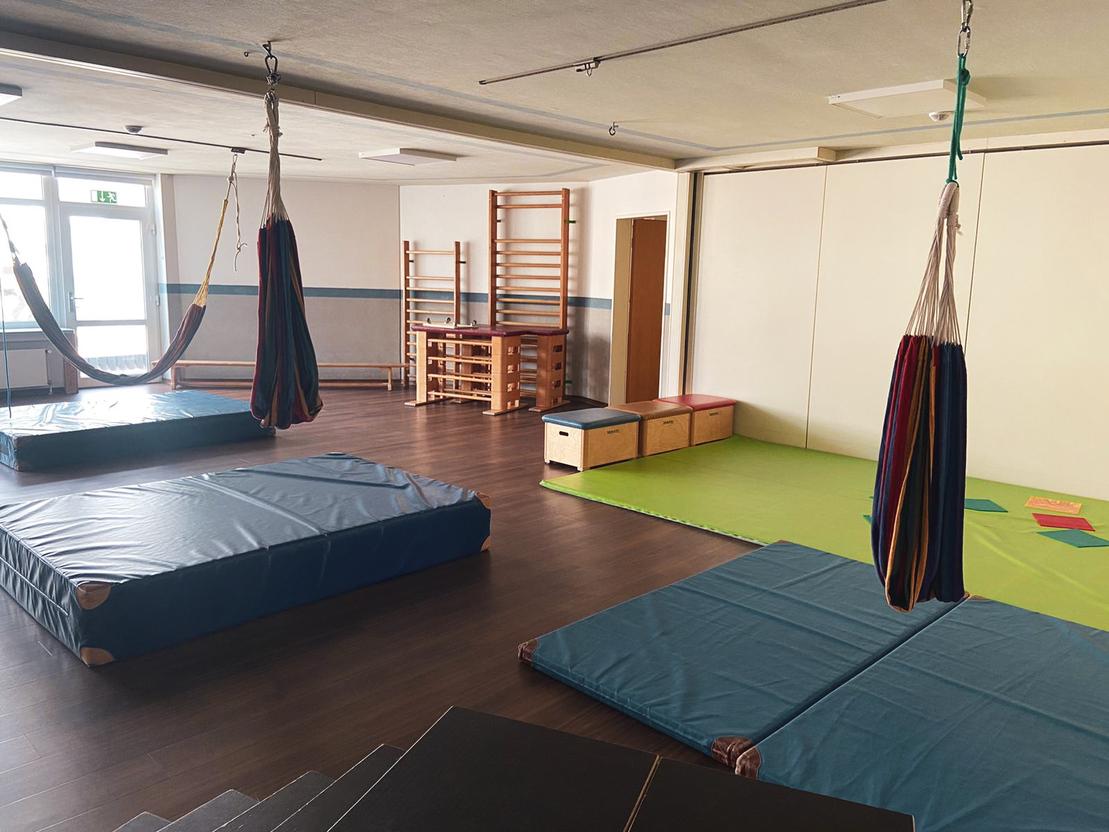 Raum mit Turnmatten, H&auml;ngematten, einer Kletterwand und einem bunten Spielbereich auf dem Boden.