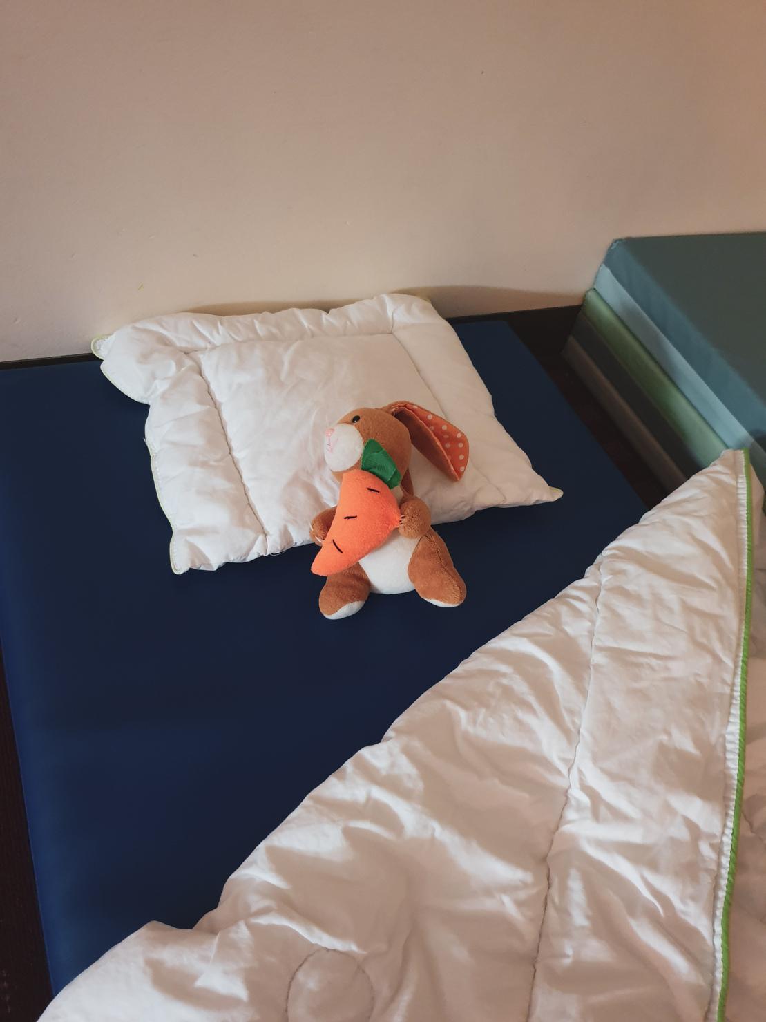Stofftier-Hase sitzt auf einem blauen Schlafuntergrund neben einem Kissen und einer Decke.