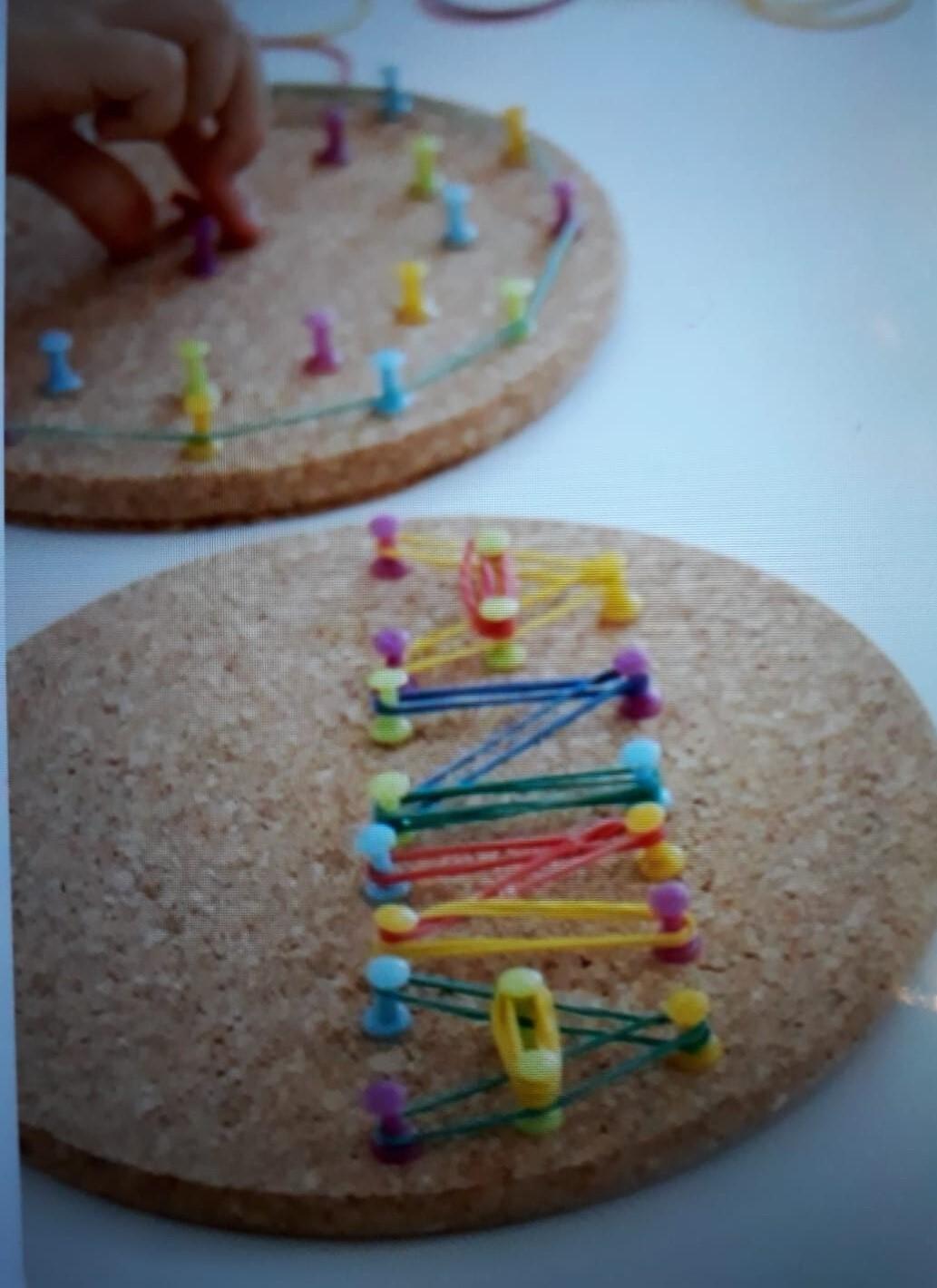 Zwei Korkplatten mit bunten Stecknadeln und Gummib&auml;ndern, eine davon wird gerade bearbeitet.