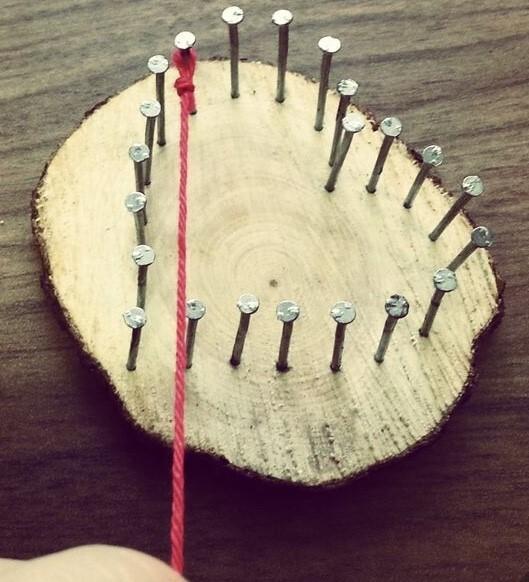 Holzscheibe mit eingelassenen N&auml;geln, an denen ein roter Faden entlanggef&uuml;hrt wird.