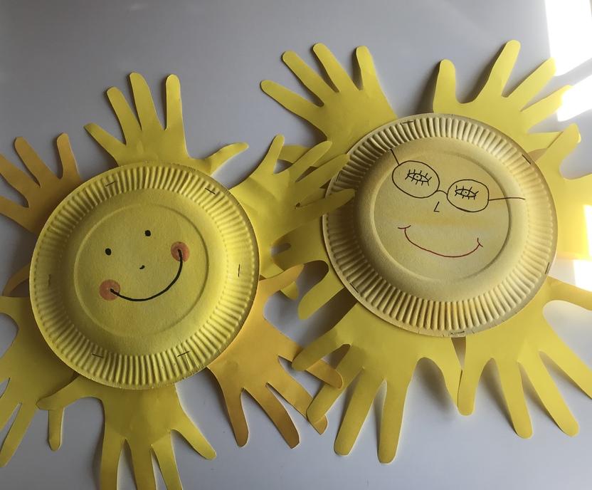 Zwei gelbe Sonnen aus Papptellern mit lachenden Gesichtern und bunten Handabdr&uuml;cken als Strahlen.
