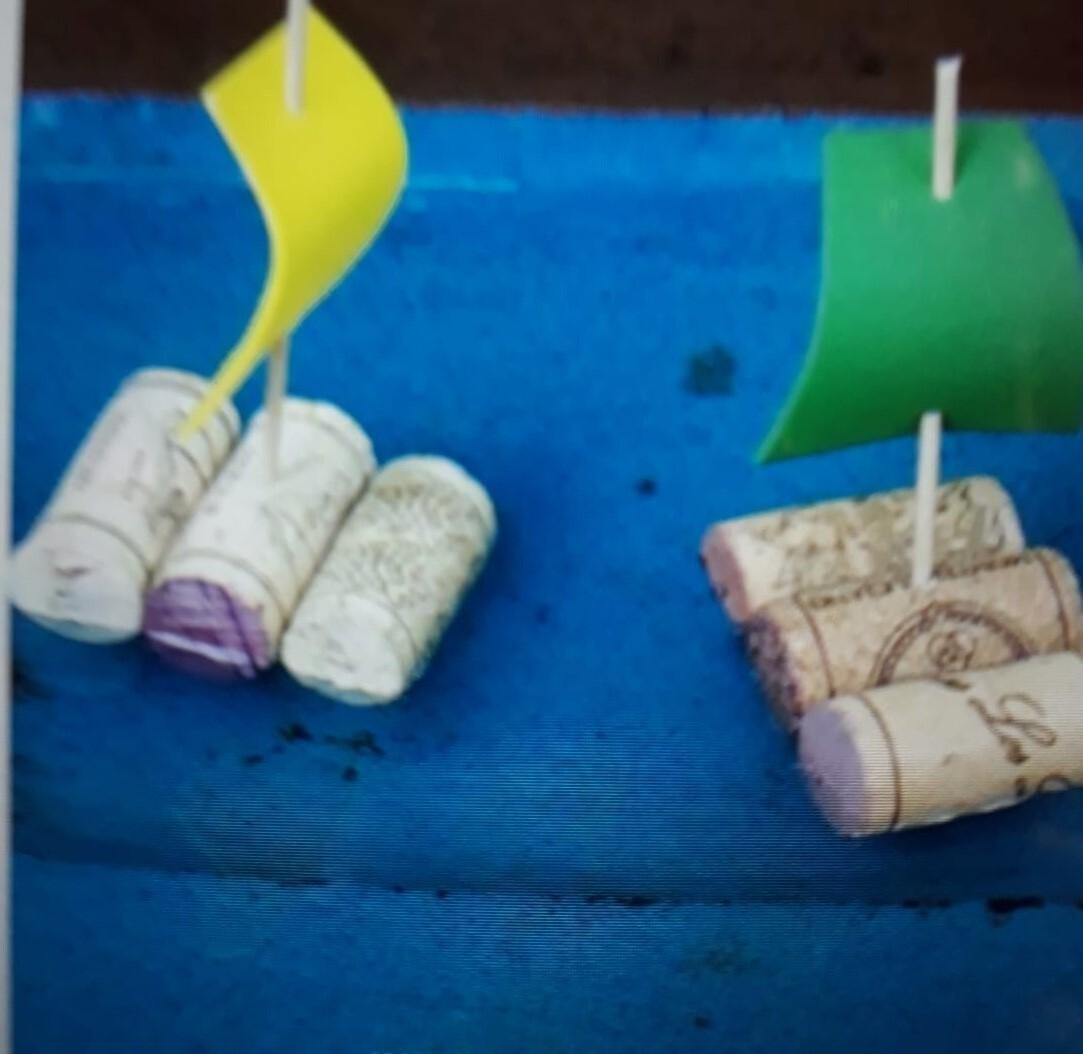 Zwei kleine Boote aus Korken mit bunten Segeln auf einer blauen Unterlage.