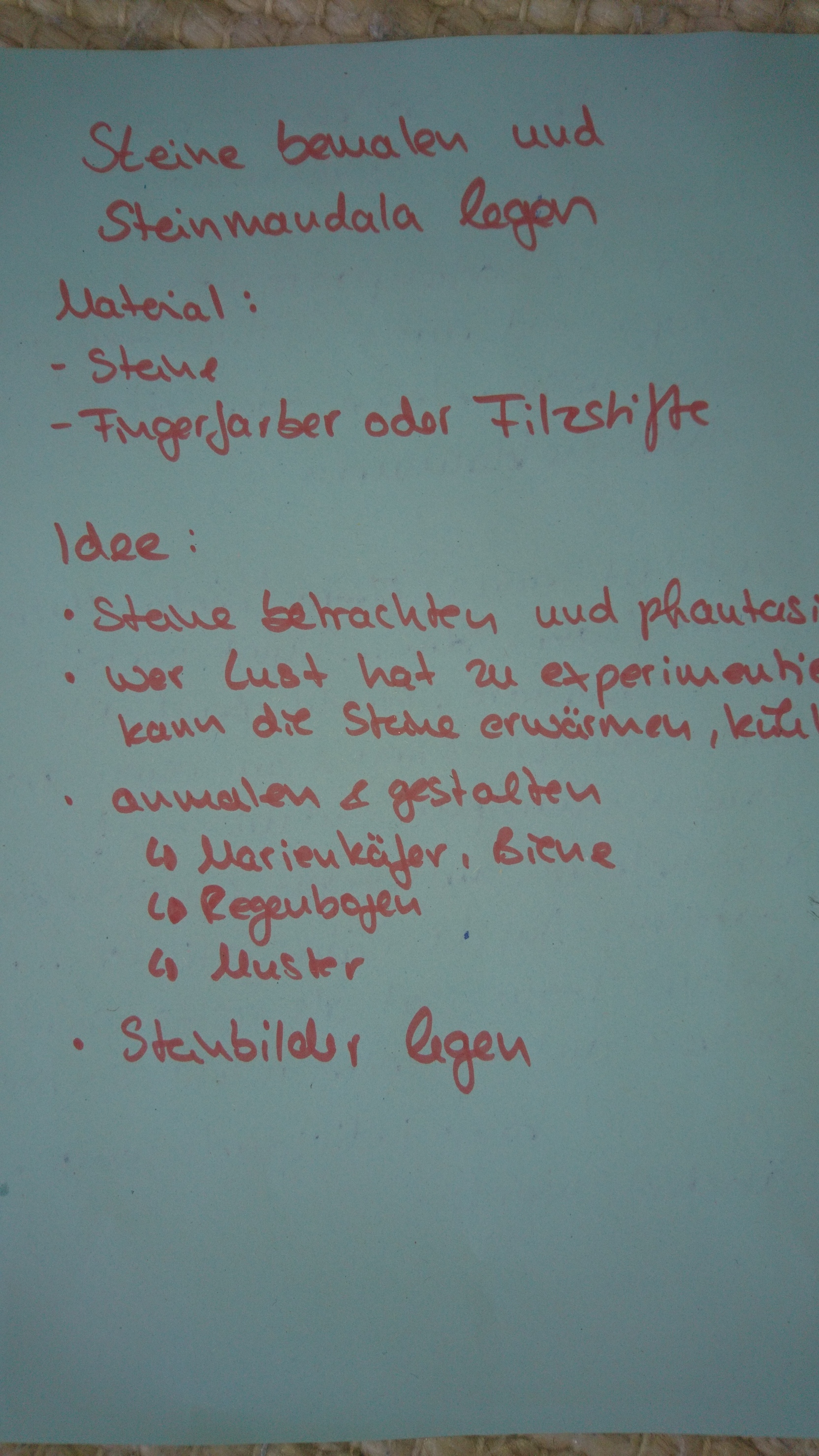 Blatt mit handschriftlichen Anleitungen zum Bemalen von Steinen und Legen von Steinmandalas in blauer Farbe.