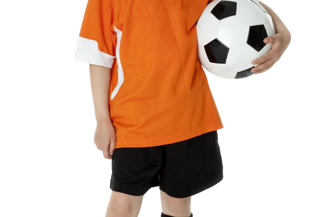 Ein M&auml;dchen in orangefarbenem Fu&szlig;balltrikot h&auml;lt einen schwarzen und wei&szlig;en Fu&szlig;ball vor einem wei&szlig;en Hintergrund.