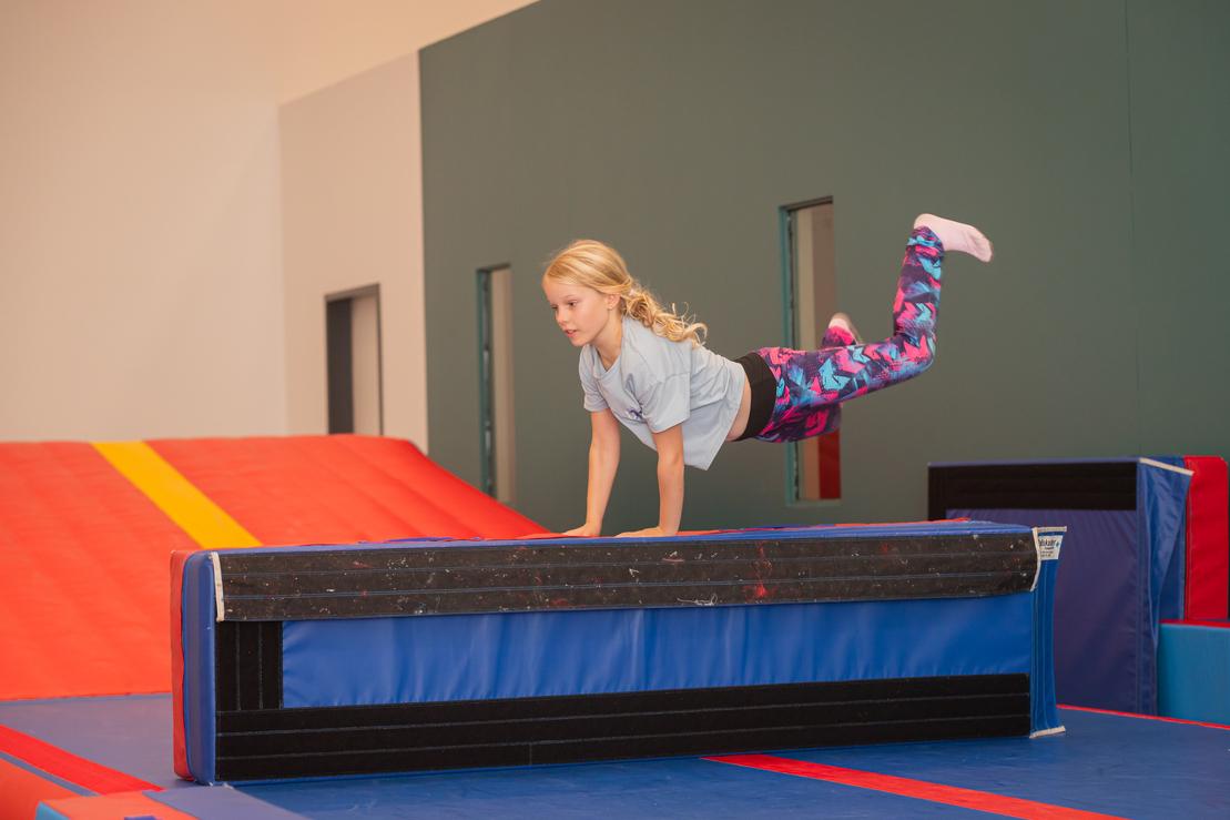 M&auml;dchen in Sportkleidung springt &uuml;ber eine Trainingsmatte in einer Turnhalle.