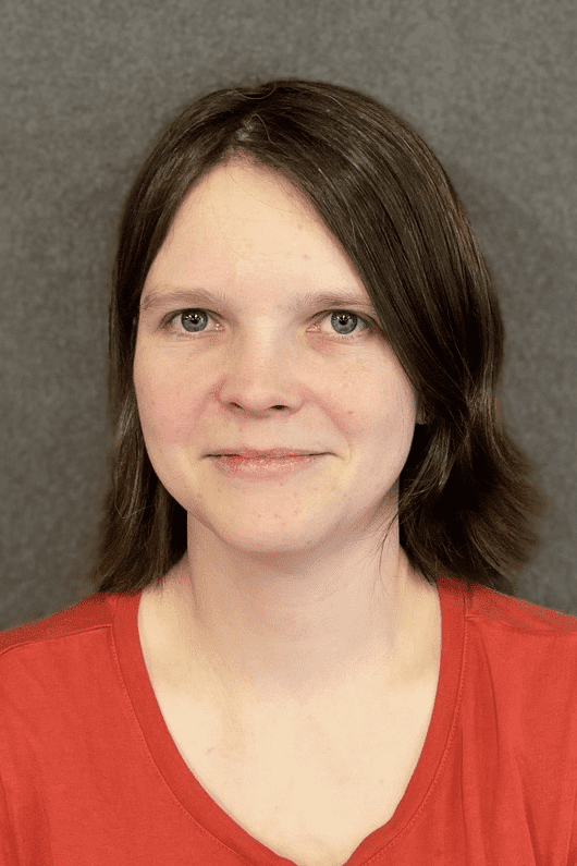 Porträt einer Person mit kurzen Haaren, die ein rotes T-Shirt trägt, vor einem grauen Hintergrund.