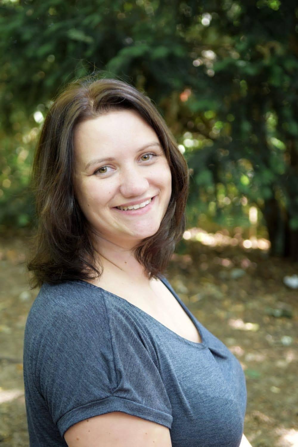 Porträt einer lächelnden Frau mit langen, braunen Haaren vor einem unscharfen, grünen Hintergrund.